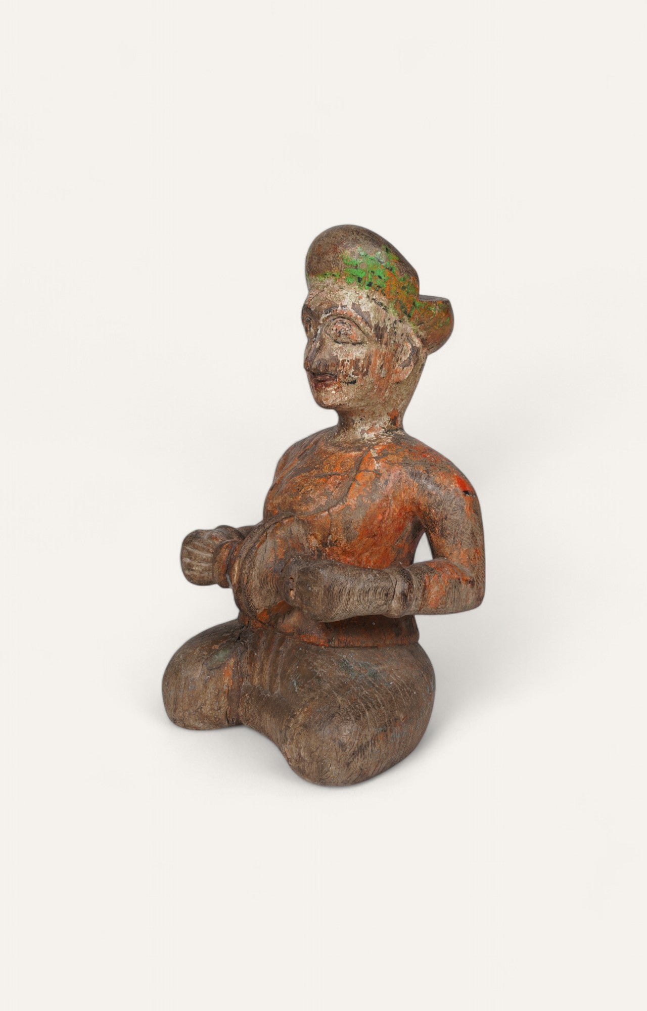 Seated teak wood folk figurine with faded red-orange patina.